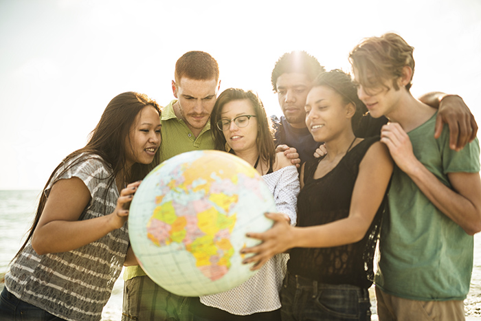 Group of diverse people of different ages and ethnicities looking at a globe together, symbolizing unity and global awareness.