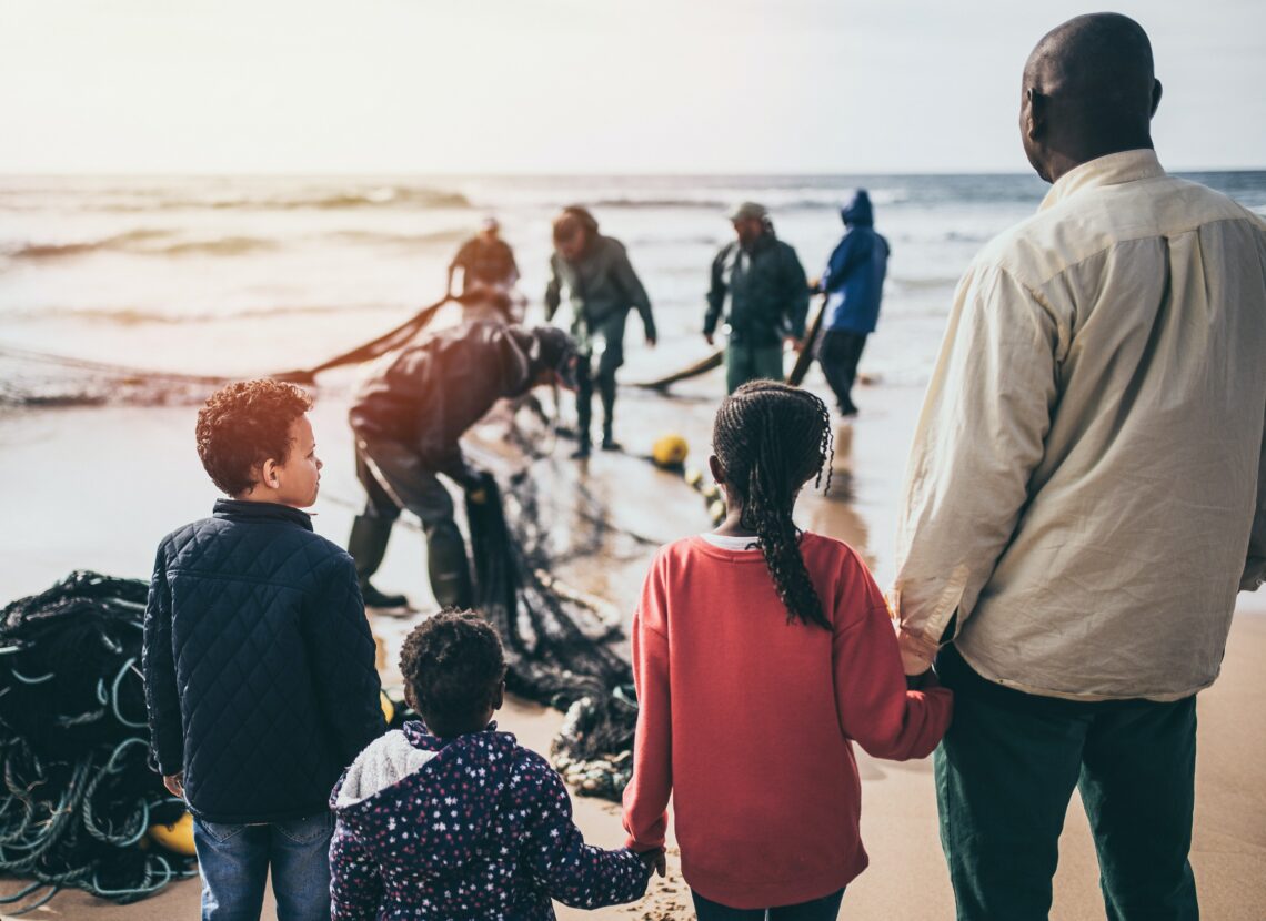 Picture of a family holding hands on a beach, three children and presumably their father.